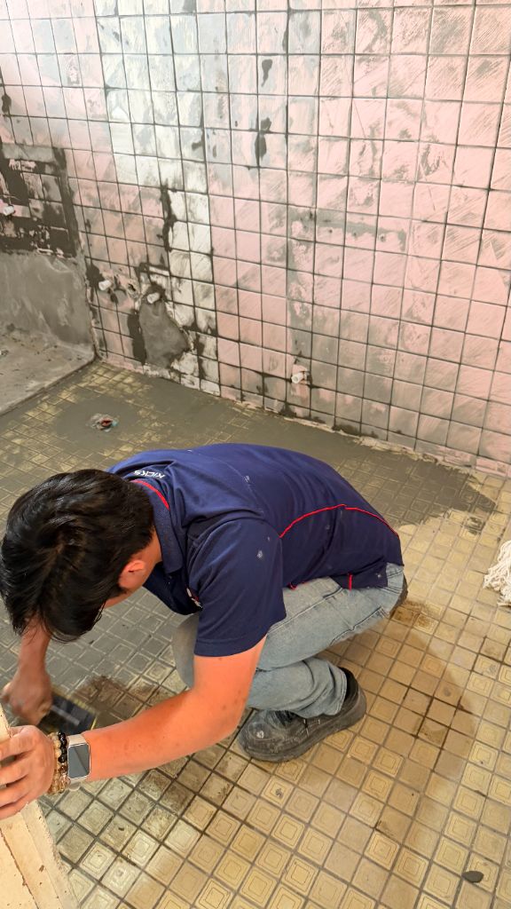 師傅進行牆面防水施作，磁磚底層刮除清整